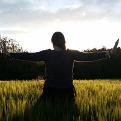 Frau steht mit ausgebreiteten Armen vor einem Feld in der Sonne